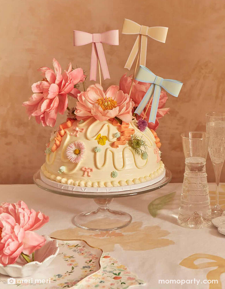 A gorgeous floral cake adorned with beautiful spring flowers and Momo Party's 3D pastel bow toppers. On the table there are Meri Meri's elegant floral plates and napkins.