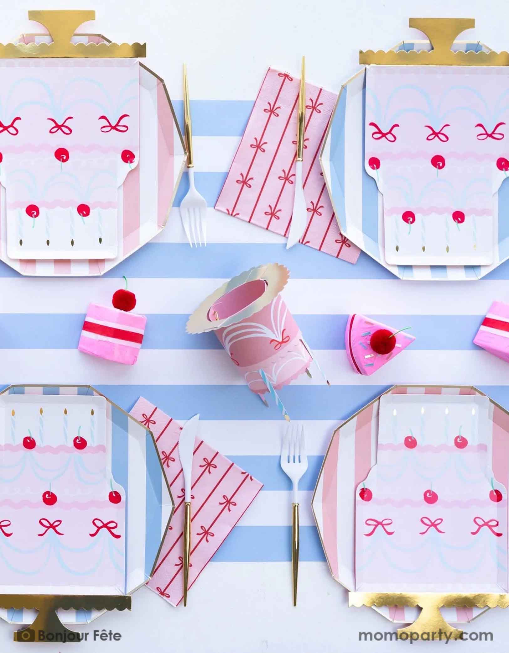 An stylish and chic birthday party table setting featuring multiple pastel blue and pink themed tableware including birthday cake shaped plates, pink bow napkins, matching cups, cabana striped blue dinner plates and pastel pink plates, gold and white utensils, all over the sky blue cabana striped table runner, making this a festive tablescape for a chic and stylish gathering.
