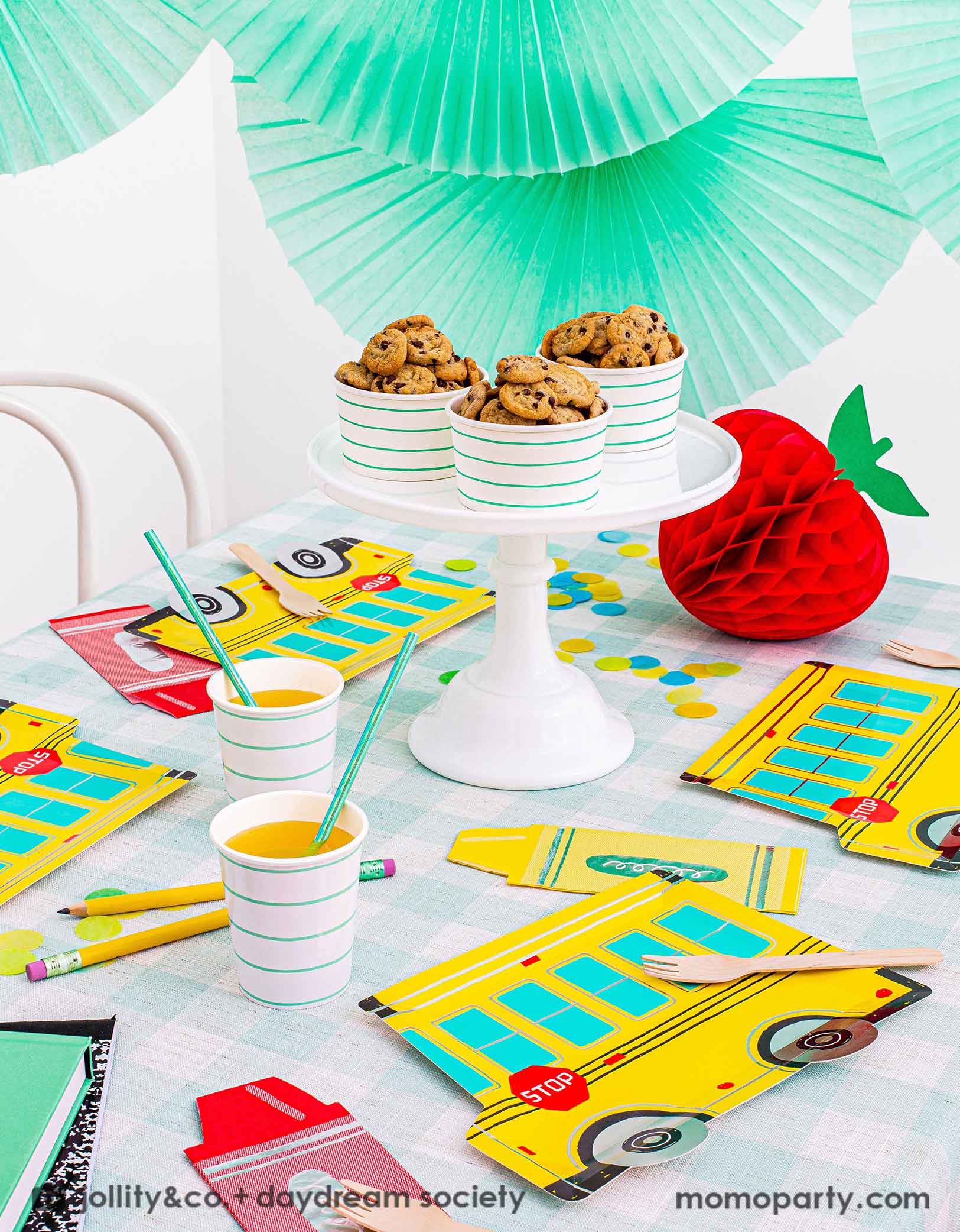 A festive back to school party featuring Momo Party's colorful school themed tableware including Daydream Society's school bus shaped plates, crayon shaped napkins with aqua striped party cups and snack cups filled with cookies, all on a mint gingham checkered tablecloth. With a festive apple shaped honeycomb decoration on the party table and mint bunting paper fans hung above the table, this gives a great idea and inspiration for a kid's back to school party or a first day of school celebration.