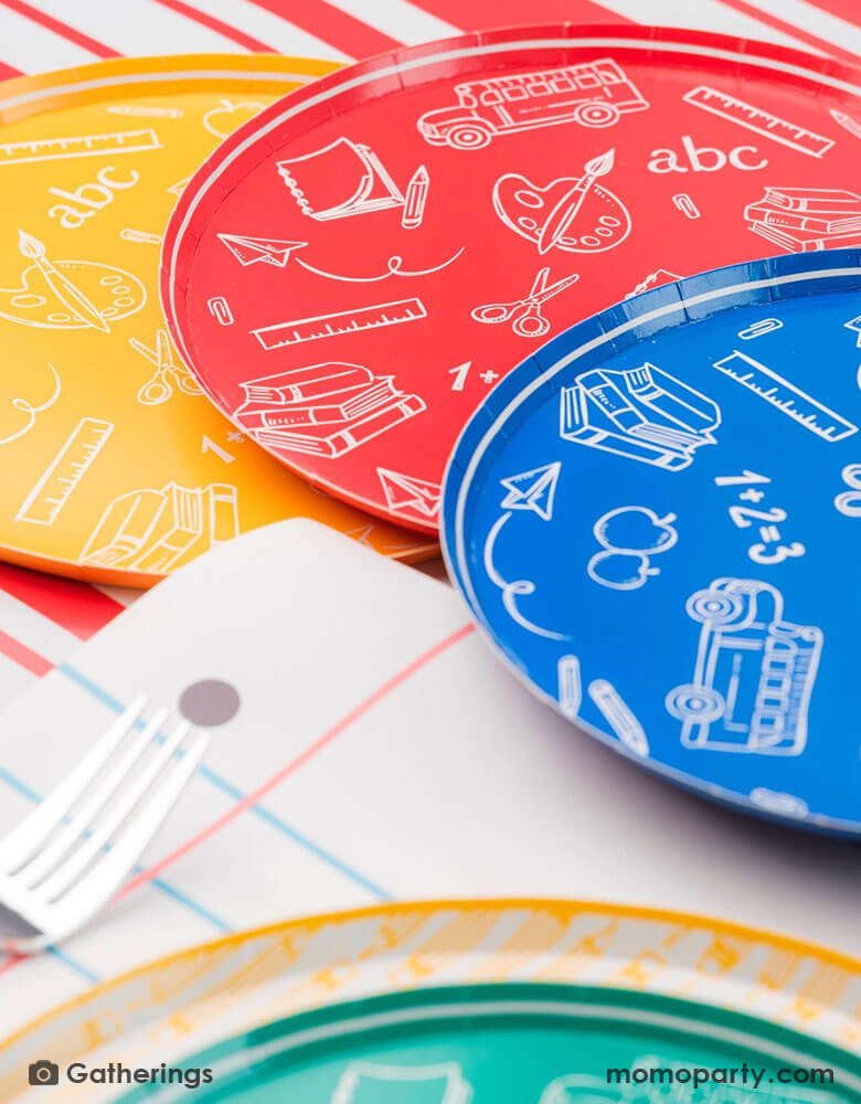 A close up of a back to school party featuring school themed party supplies from Momo Party including school day assorted side plates with school supply patterns in 4 colors of green, blue, red and yellow, with the No. 2 pencil patterned dinner plates and loose leaf paper placemats by Gatherings. A perfect place setting to celebration kid's or student's first day of schoo,