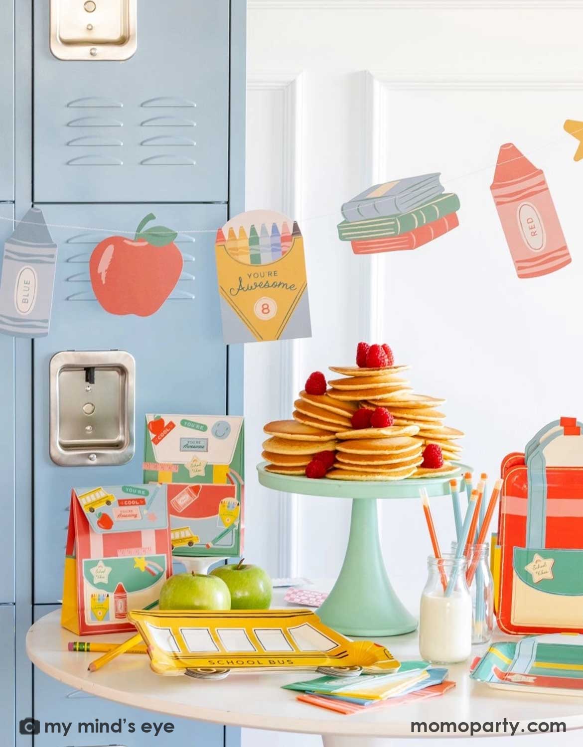 A close-up shot of a back to school classroom set up featuring various school themed party supplies and decors from Momo Party including school themed plates, treat boxes, party pennant, back to school felt garland along with school icons party banner hung above the light blue locker selves. A party table with pancakes on a cake stand next to some colorful backpack shaped treat bags.