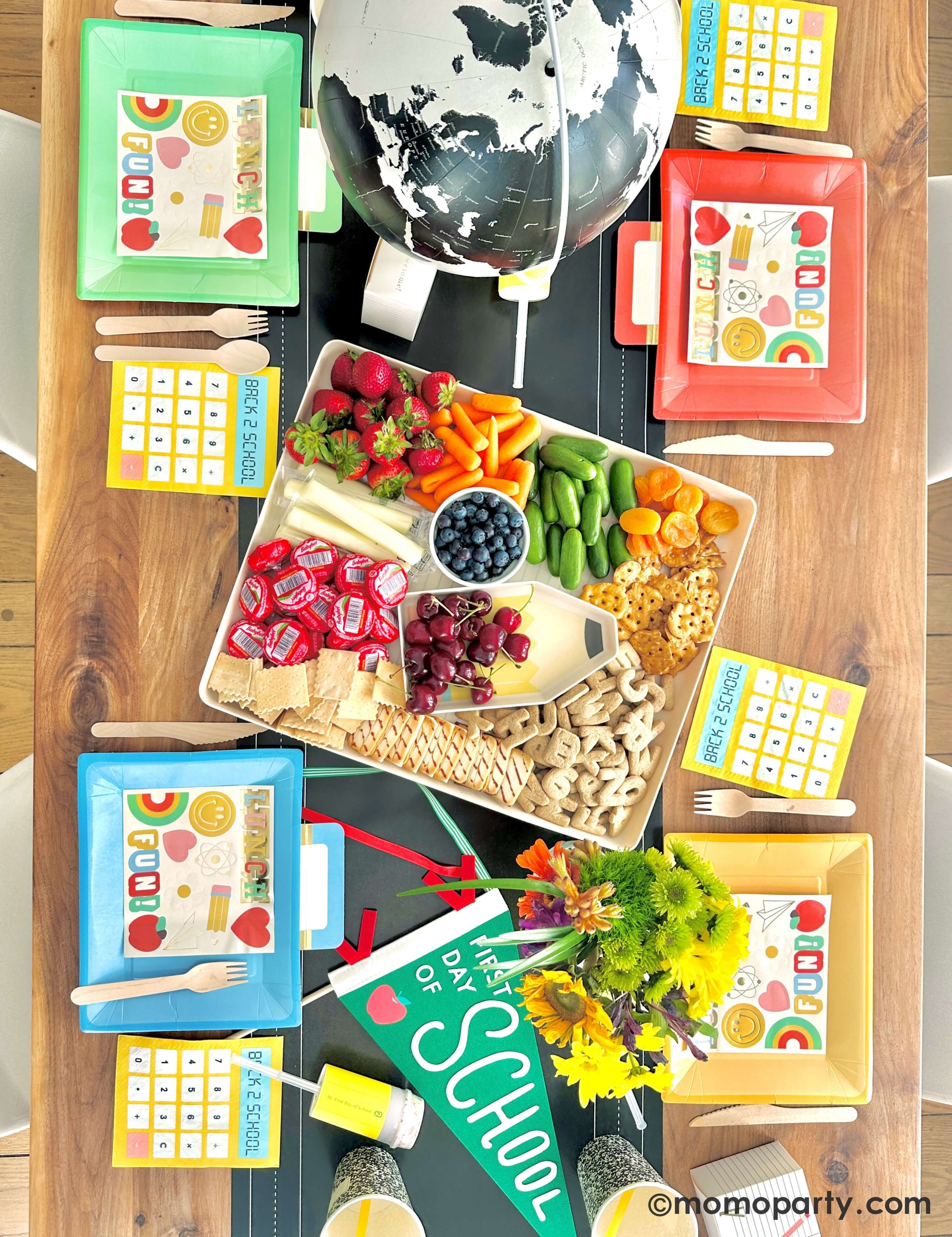 Topview of Kid's Back to School Celebration table set with a snack platter, lunch bag shaped plates, calculator napkins, Global, snack plater and 'First Day of School' sign.