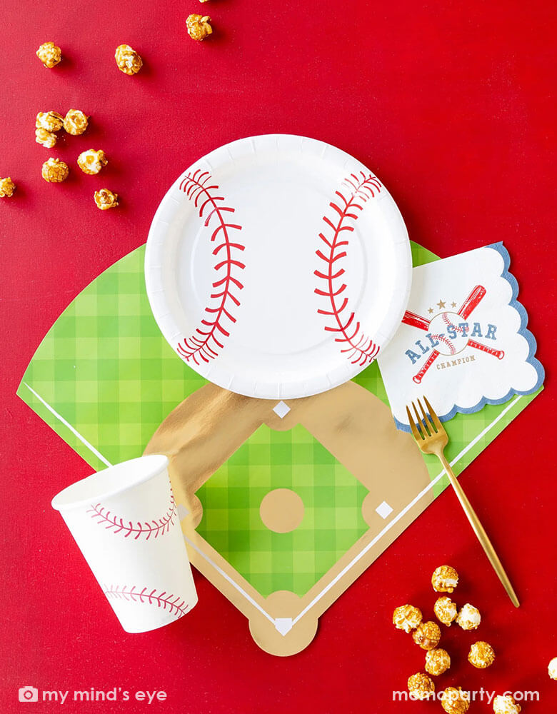 Momo Party's baseball party collection on a red table featuring baseball paper tableware by My Mind's Eye, including baseball shaped plates, 5"x 5" baseball all star small napkins, baseball field shaped placemats, and baseball party cups, along with some popcorn around these partyware, this makes a great inspiration for a fun kid's baseball themed birthday party or a championship celebration!