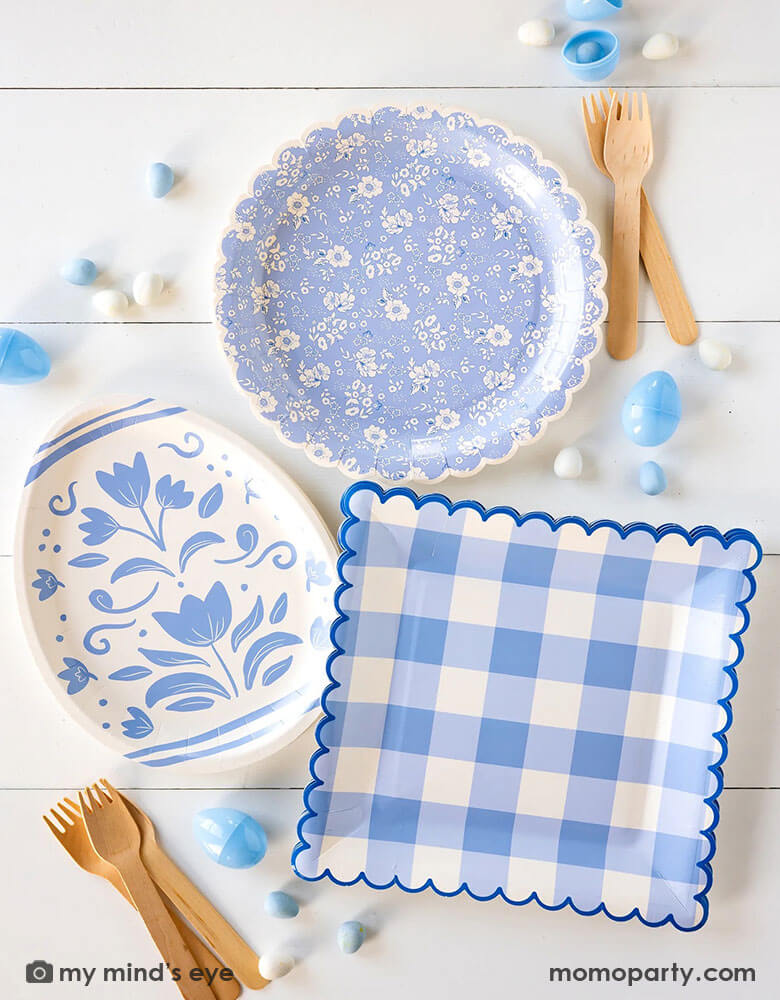 An overhead shot of a beautiful Easter party tablescape featuring Momo Party's Easter themed party supplies in light blue including the floral egg shaped plate, blue ditsy floral scallop plate and the blue gingham large plate, with blue Easter eggs and egg shaped candies spread out - a perfect inspo for an elegant Easter celebration.