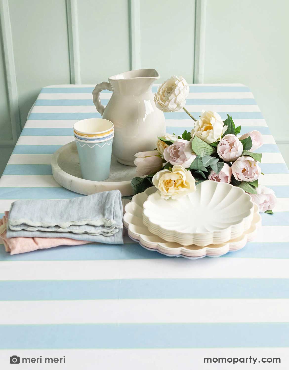 An elegant and clean table setting with Meri Meri's pastel party plates, cups and napkins from Momo Party and spring flowers on Momo Party's pale blue striped tablecloth. A modern and simple idea for spring or Easter party table setting.