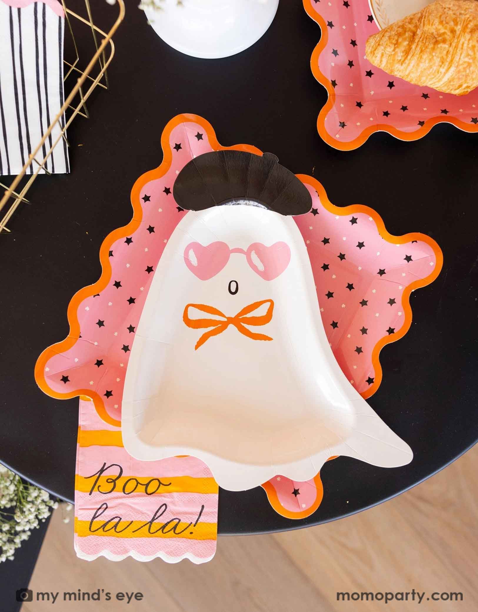 A pink Halloween party table featuring Momo Party's Boo La La ghost themed party tableware by My Mind's Eye including the ghost diecut shaped plate, the pink star striped dinner plates, the orange and pink striped dinner napkin with 'Boo la la!' text. A chic and sweet Halloween party tablescape.