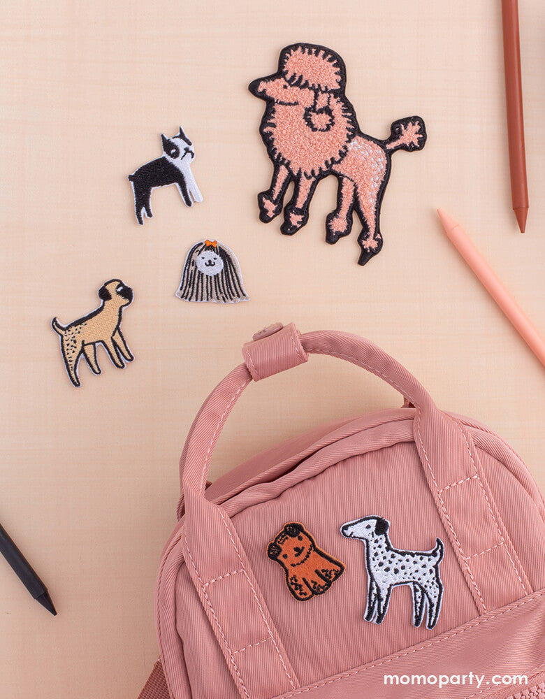 A pink backpack on the table with pencils around, with Bow Wow Patch Set from Jollity & Co Party Boutique - Daydream society- Bow Wow collection. Featuring five fun and furry puppy dogs, these patches are definitely in show! Stick these puppies on a jean jacket, pencil bag, backpack, and more!
