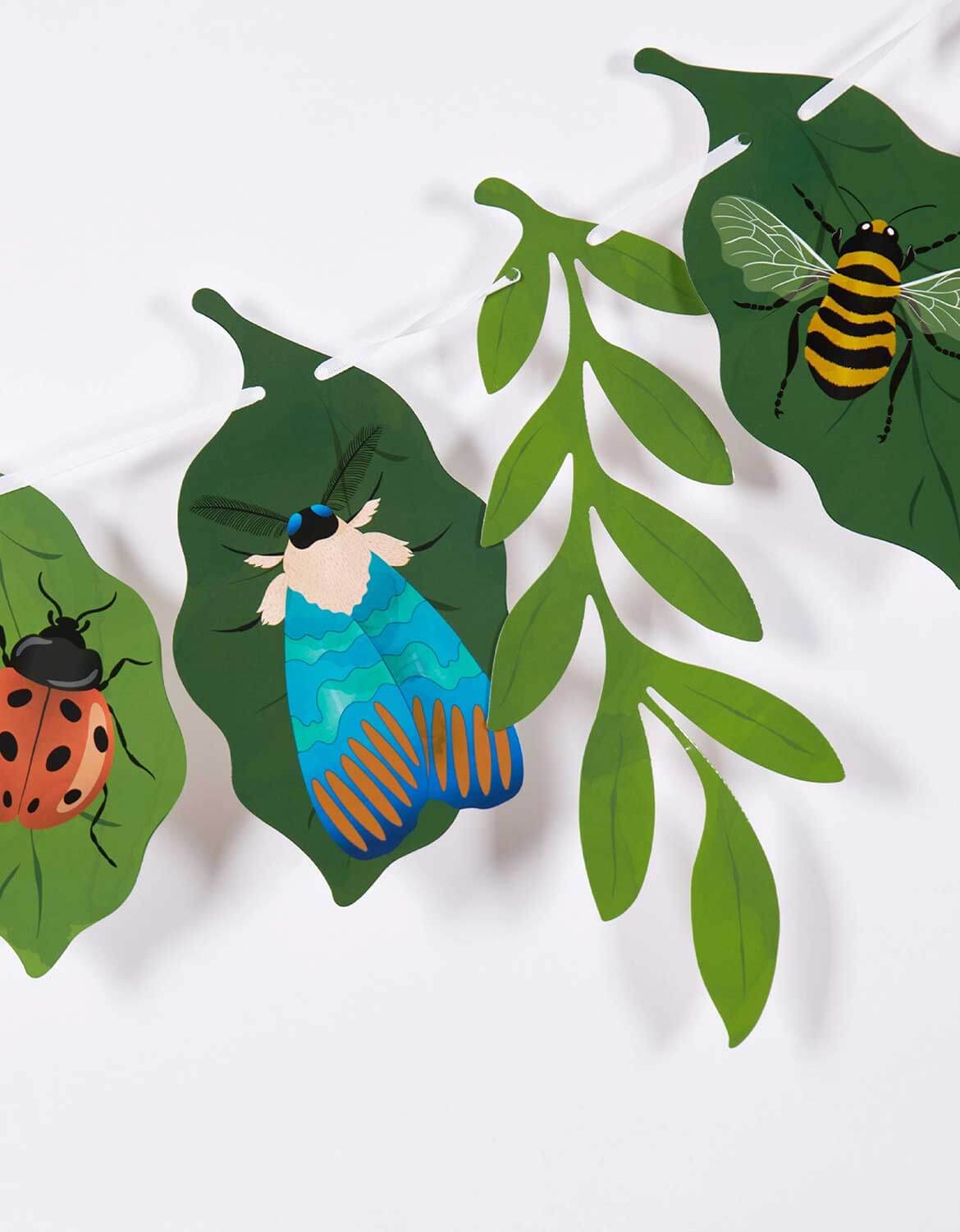A closeup shot of Momo Party's bugs themed party garland with leaf and insect designed paper pennants on a white background.