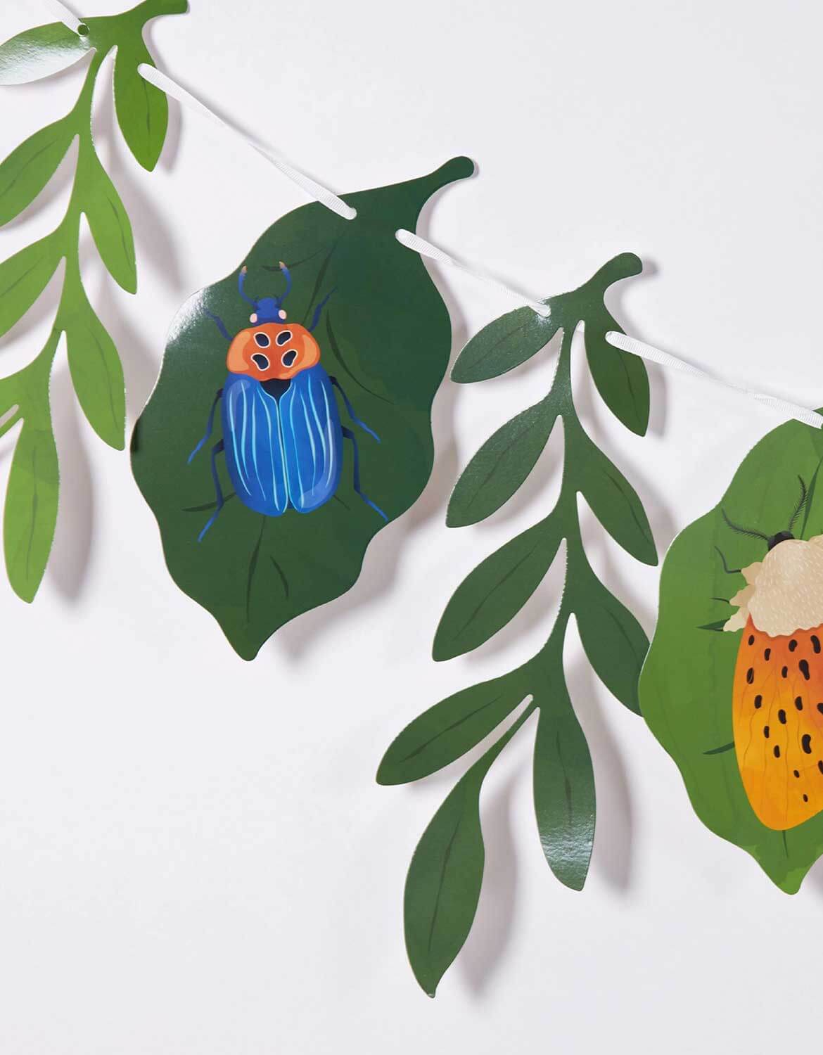 A closeup shot of Momo Party's bugs themed party garland with leaf and insect designed paper pennants on a white background.