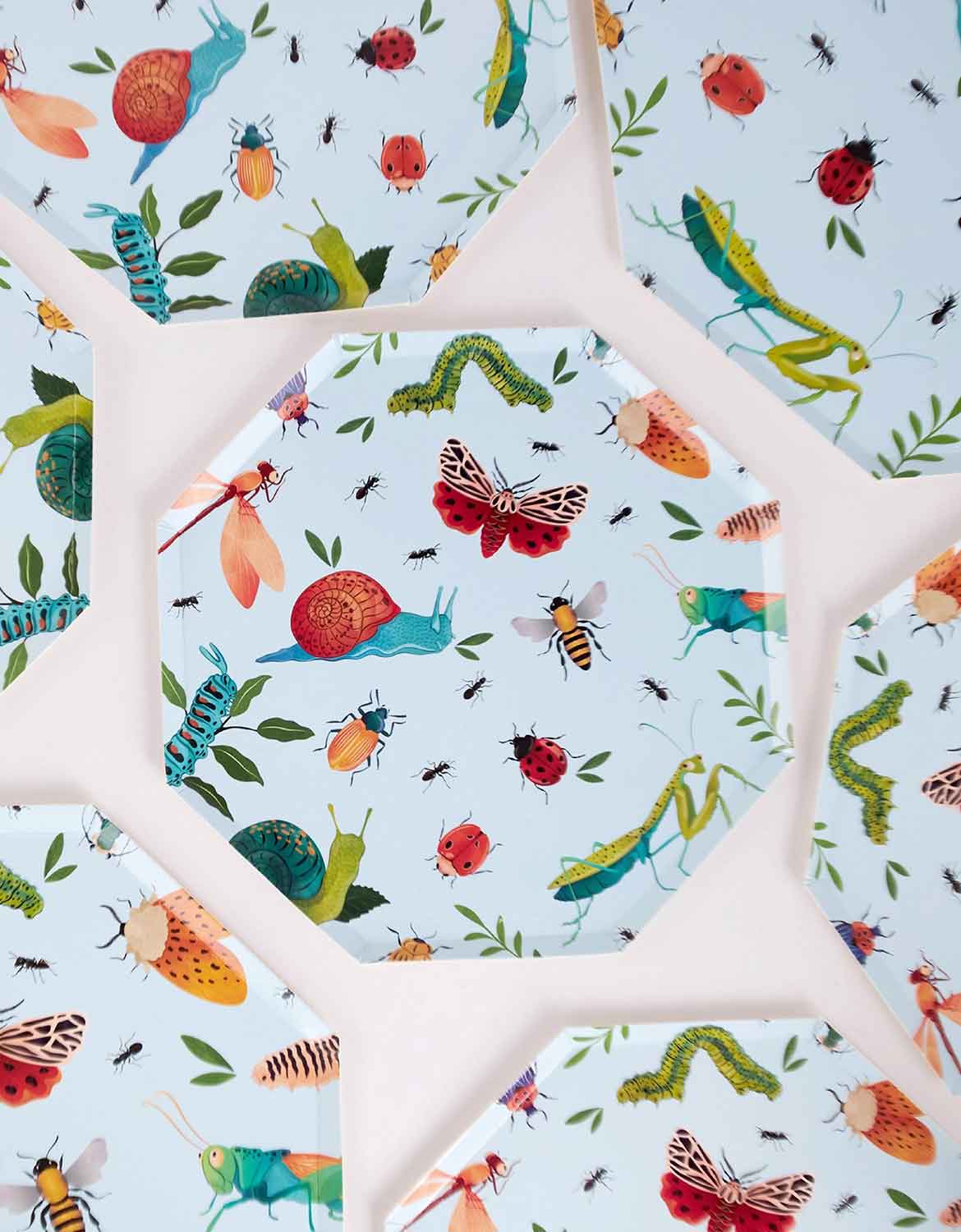 Multiple Momo Party's 10" light blue hexagonal party plates with colorful insect pattern spread out on a white background.
