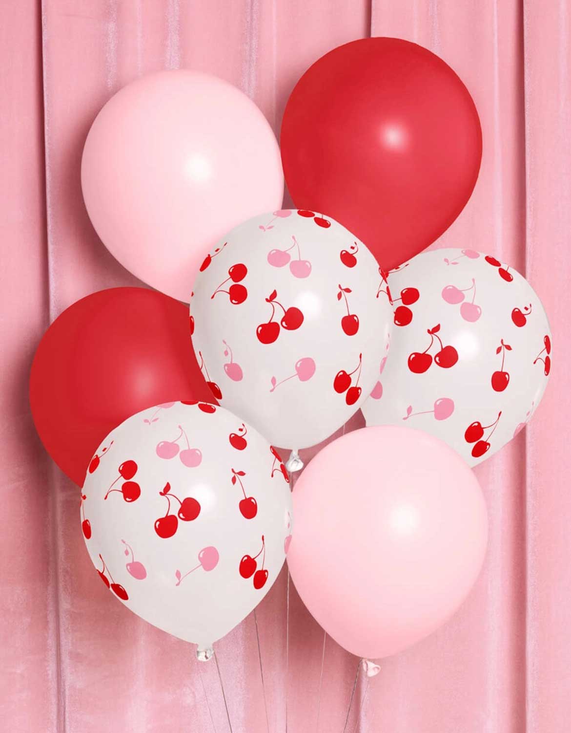 Momo Party's Cherry Print Latex Balloon Mix with red, pink and cherry pink balloons floating against a pink curtain.