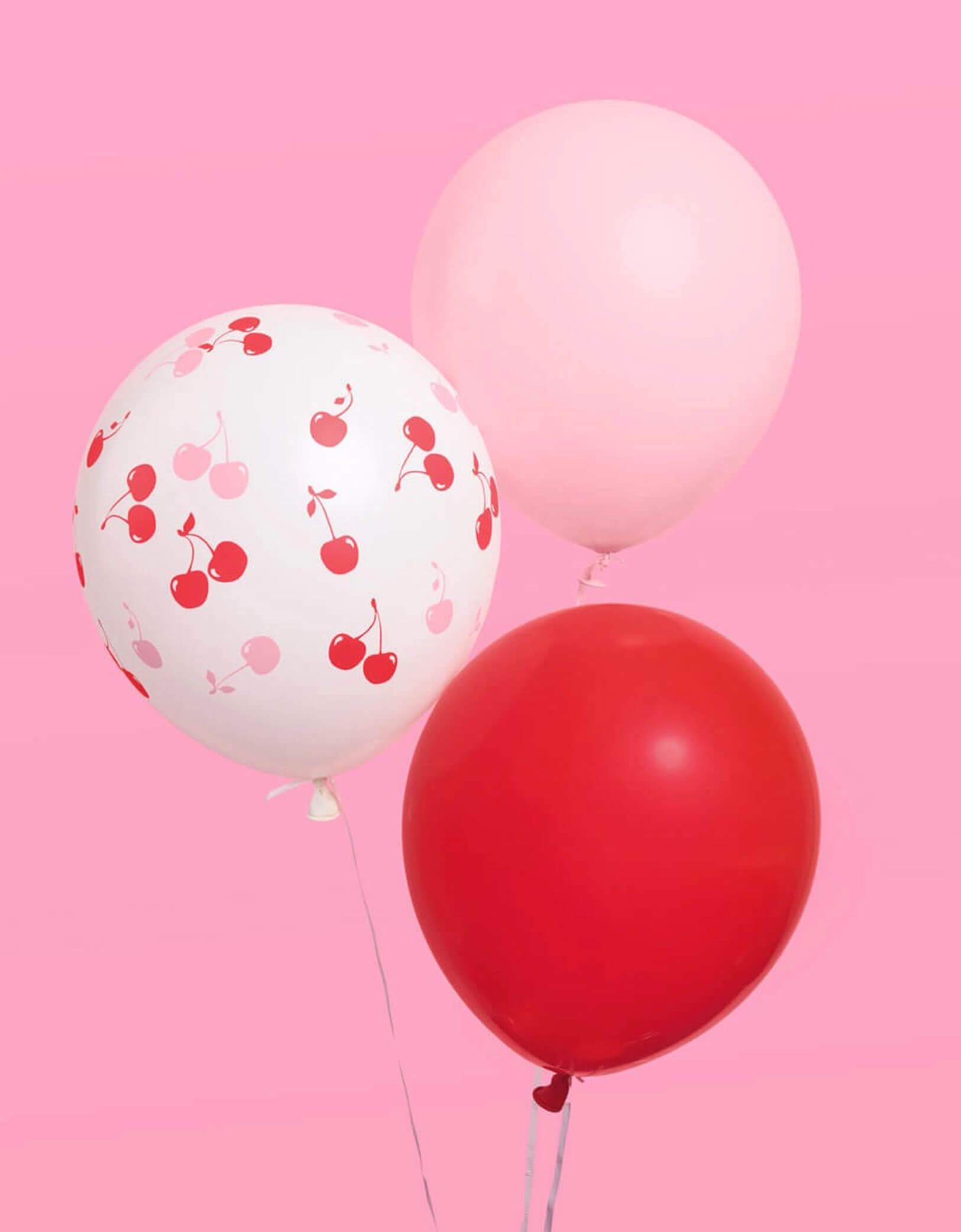 Momo Party's Cherry Print Latex Balloon Mix with red, pink and cherry pink balloons floating on a pink background.