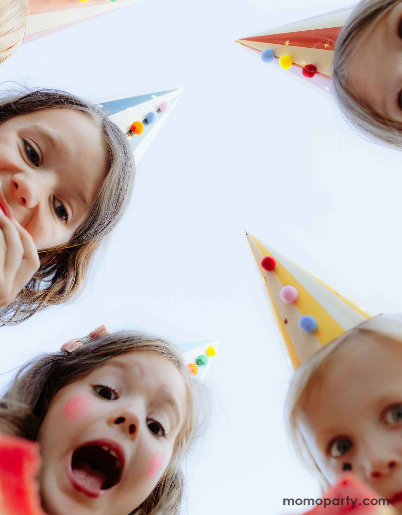 A bunch of kids dressed dressed in the vintage circus outfits and makeup wearing Momo Party's festive colorful party hats with pom poms looking into the camera and making funny faces. This set of 6 party hats features vibrant stripes in 6 different colors and colorful pom poms, adding a touch of carnival magic to any event.