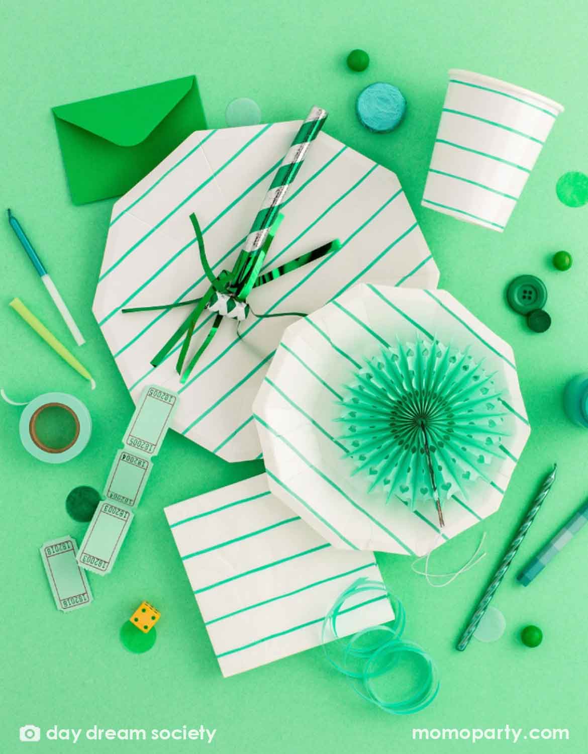 An overhead shot of Momo Party's green striped party supplies including party plates, napkins, party cups, candles, paper fans, confetti and green colored treats scattered around against a light green background.