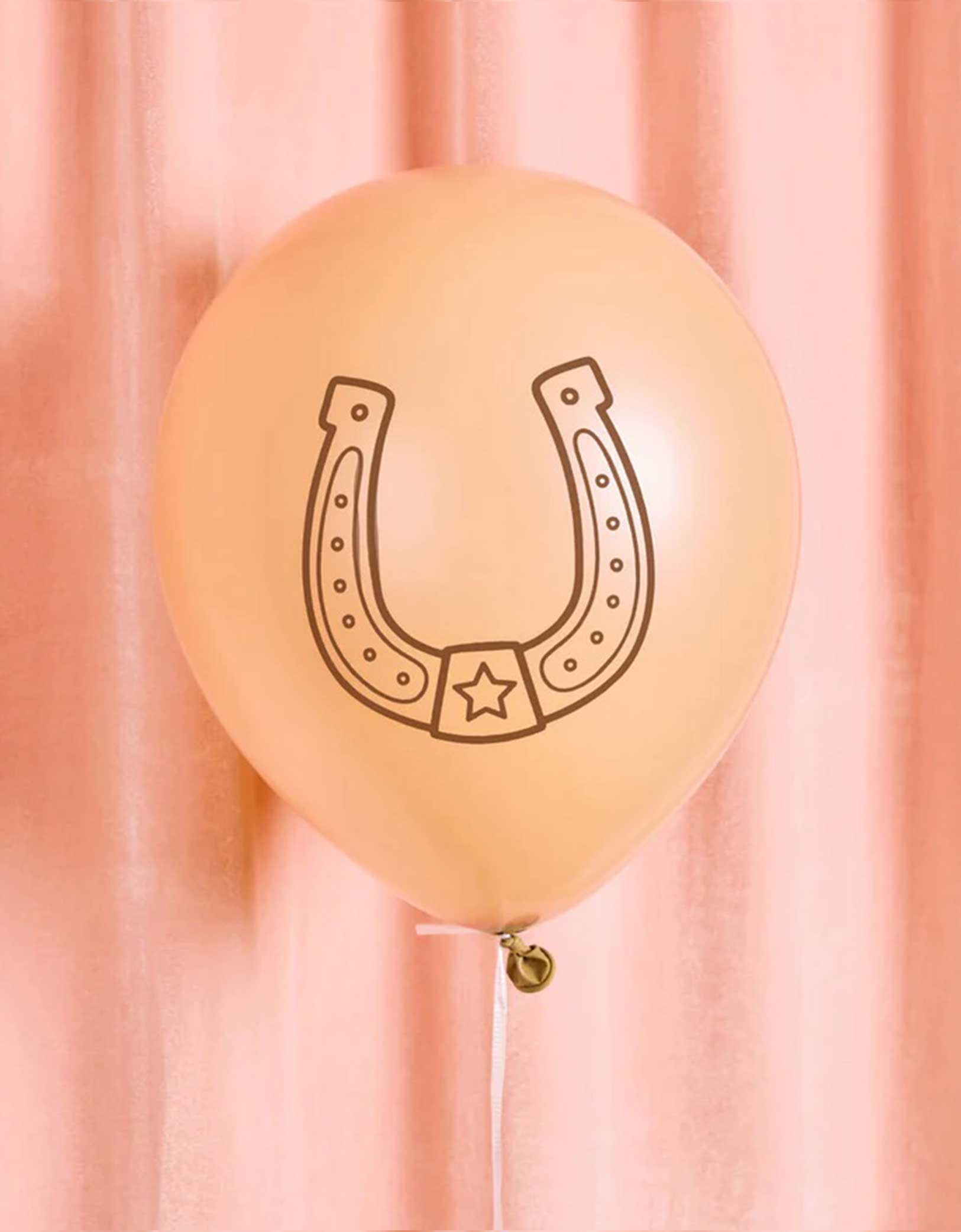 A 12" beige latex balloon with a horseshoe design from Momo Party on a pink curtain background.