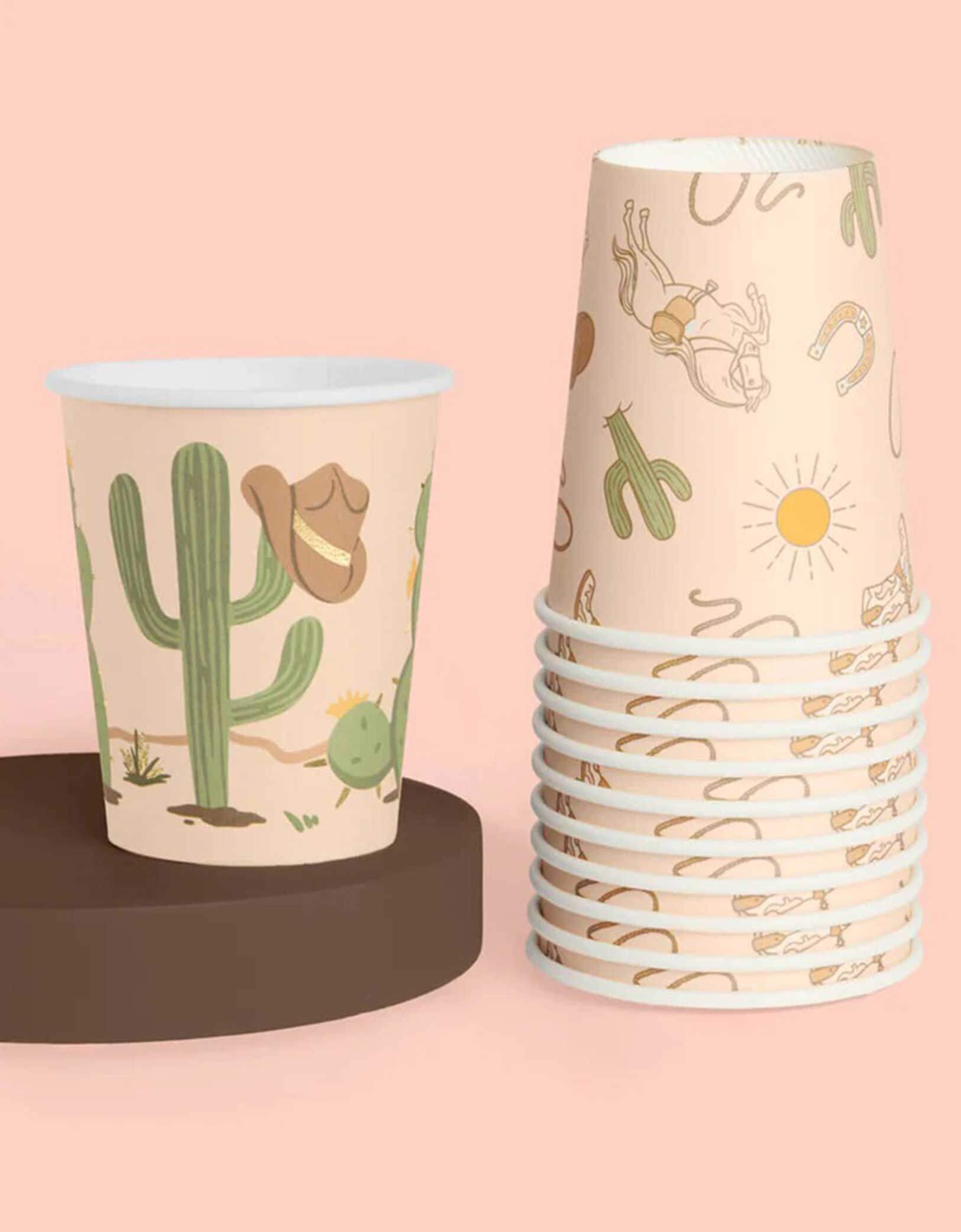 A stack of Momo Party's Wild Wild West Party Cups with Western desert-themed designs including cactus, cowboy hat, horseshoe and cowboy boots on a pink background.on a pink background.