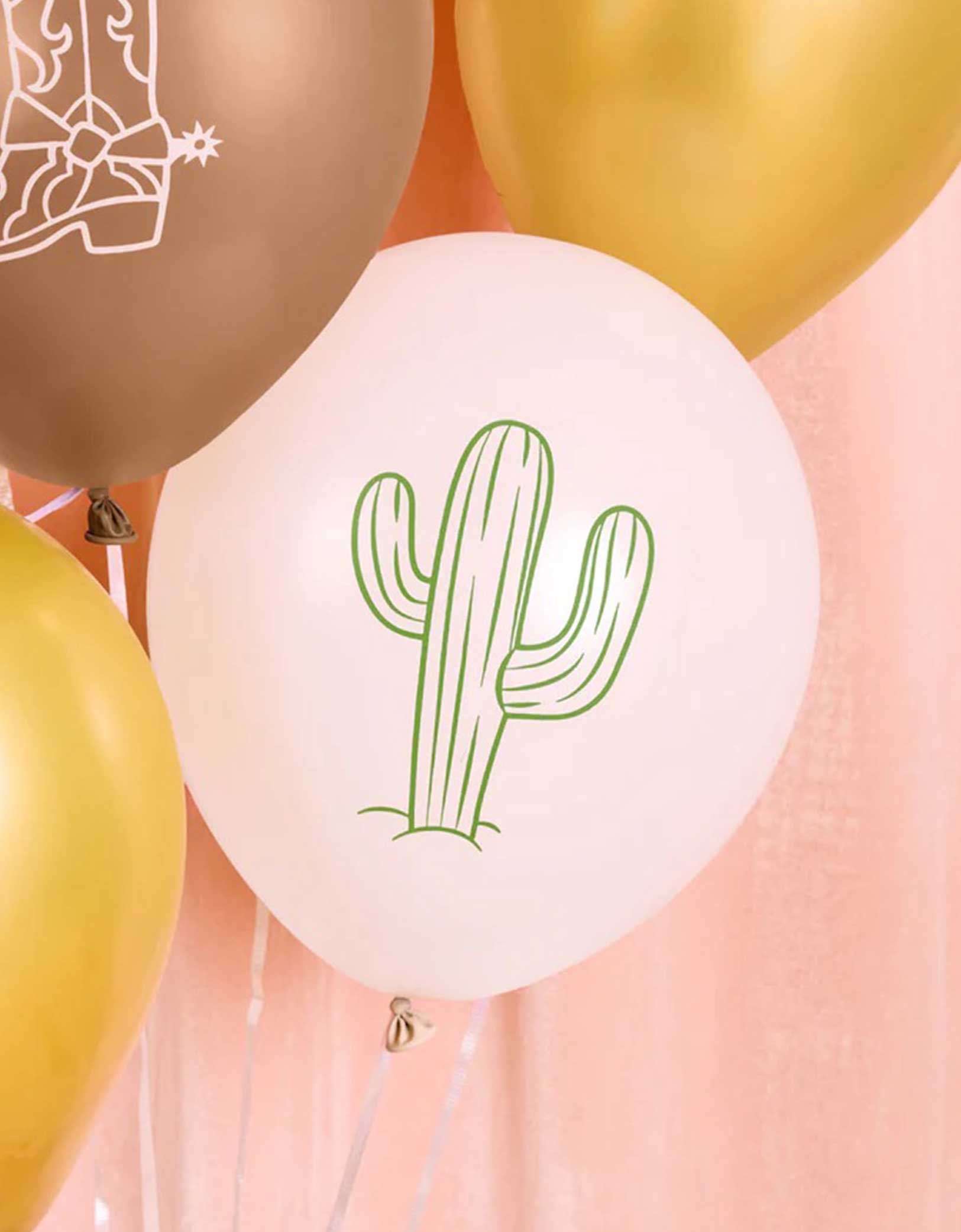 A white 12" latex balloon with green cactus design among gold and brown balloons from Momo Party on a pink background.