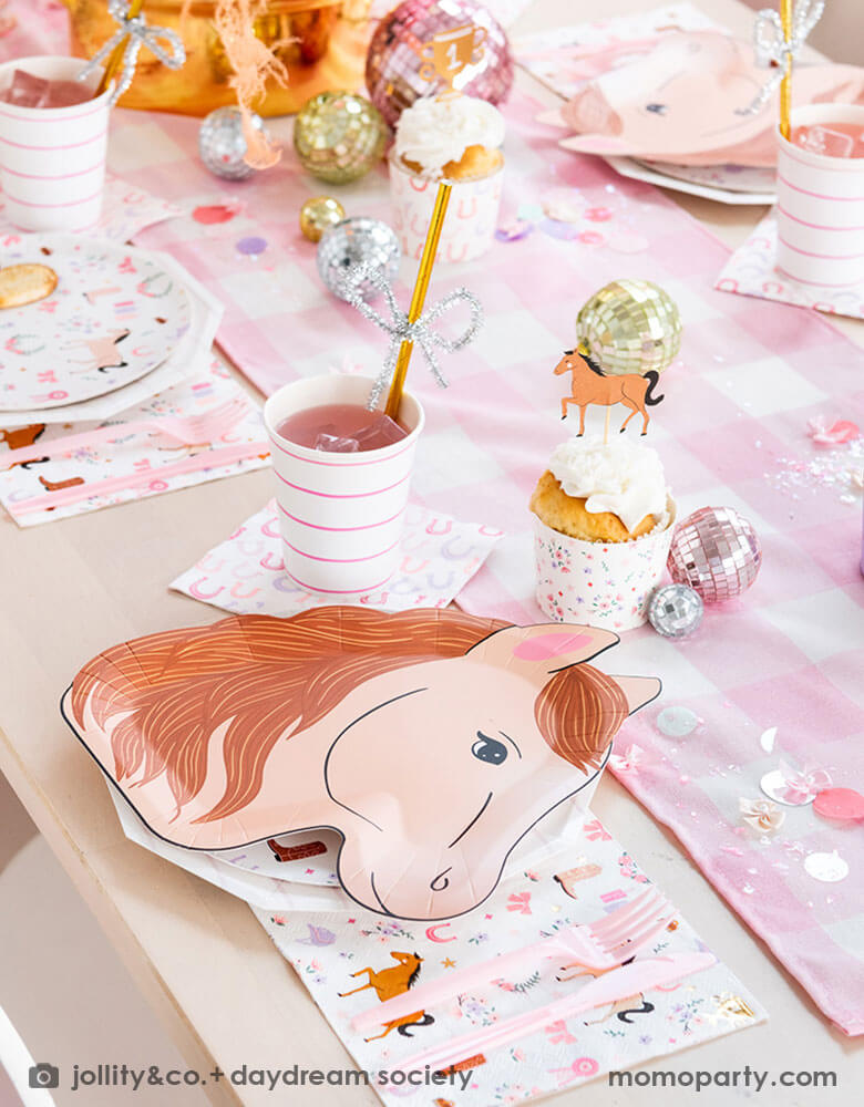 A cowgirl pony themed birthday party table featuring Momo Party's 9" x 11" pony shaped plates, cowgirl motif side plates and napkins by Daydream Society. In the middle of the party table there's a pink gingham patterned linen runner with disco ball decorations, cupcakes topped with pony shaped cake toppers and pink flower bouquet , making this a perfect party table setting idea for a girly pony / western cowgirl themed celebration.