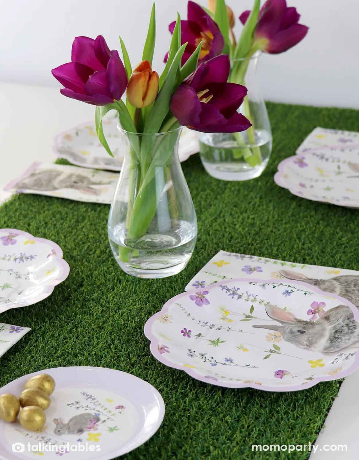 Easter-themed table setting with bunny-printed plates and napkins arranged on Momo Party's artificial grass table runner, with purple tulips in clear glass vases.