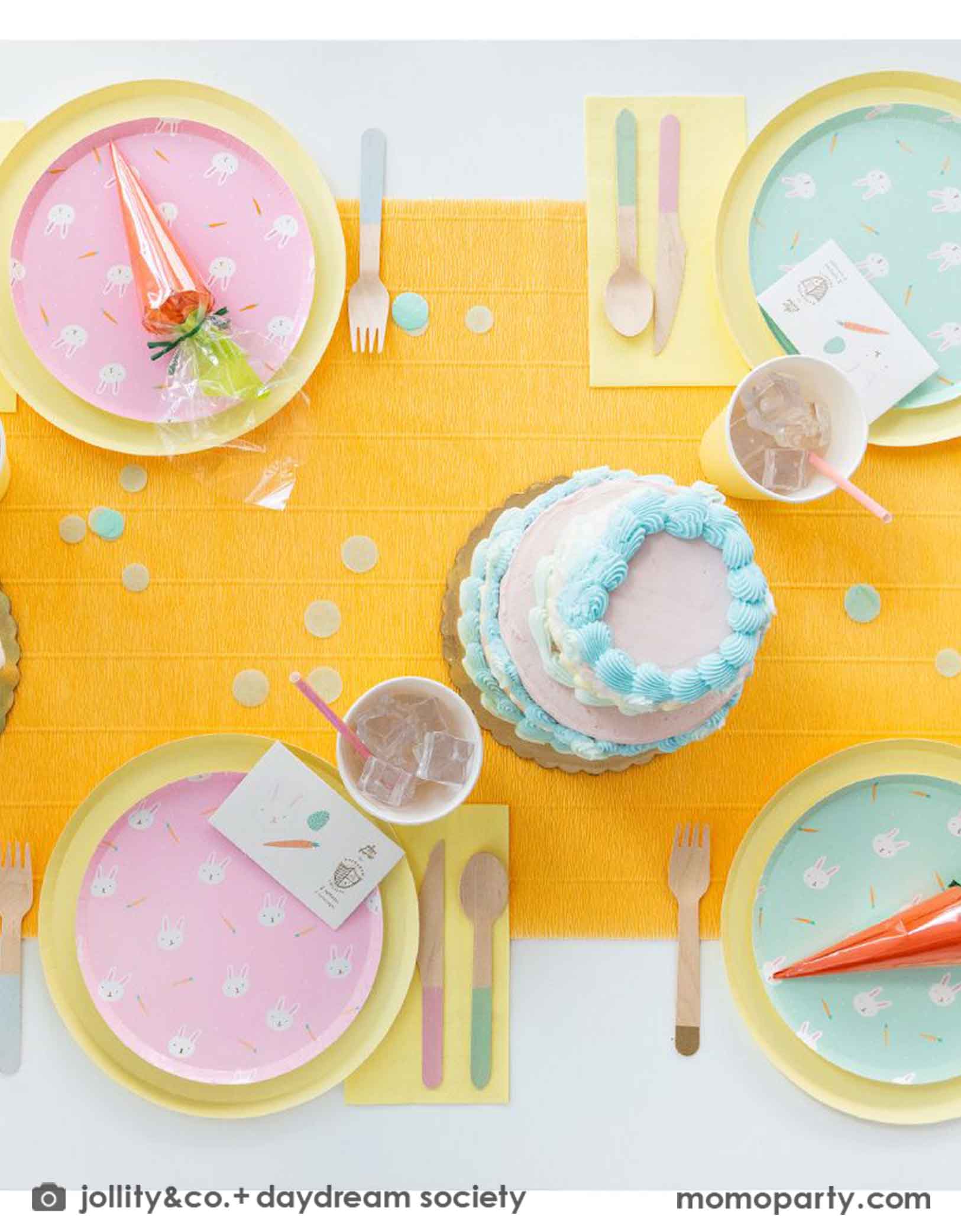 A kid's Easter party table featuring Momo Party's Easter Fun party collection by Daydream Society including Easter Fun plates in mint and pink, Easter Fun temporary tattoos, pale yellow dinner plates and party cups. On the table there are two vintage inspired buttercream cakes with pastel piping, making this a perfect inspiration for Easter brunch hosting occasion!