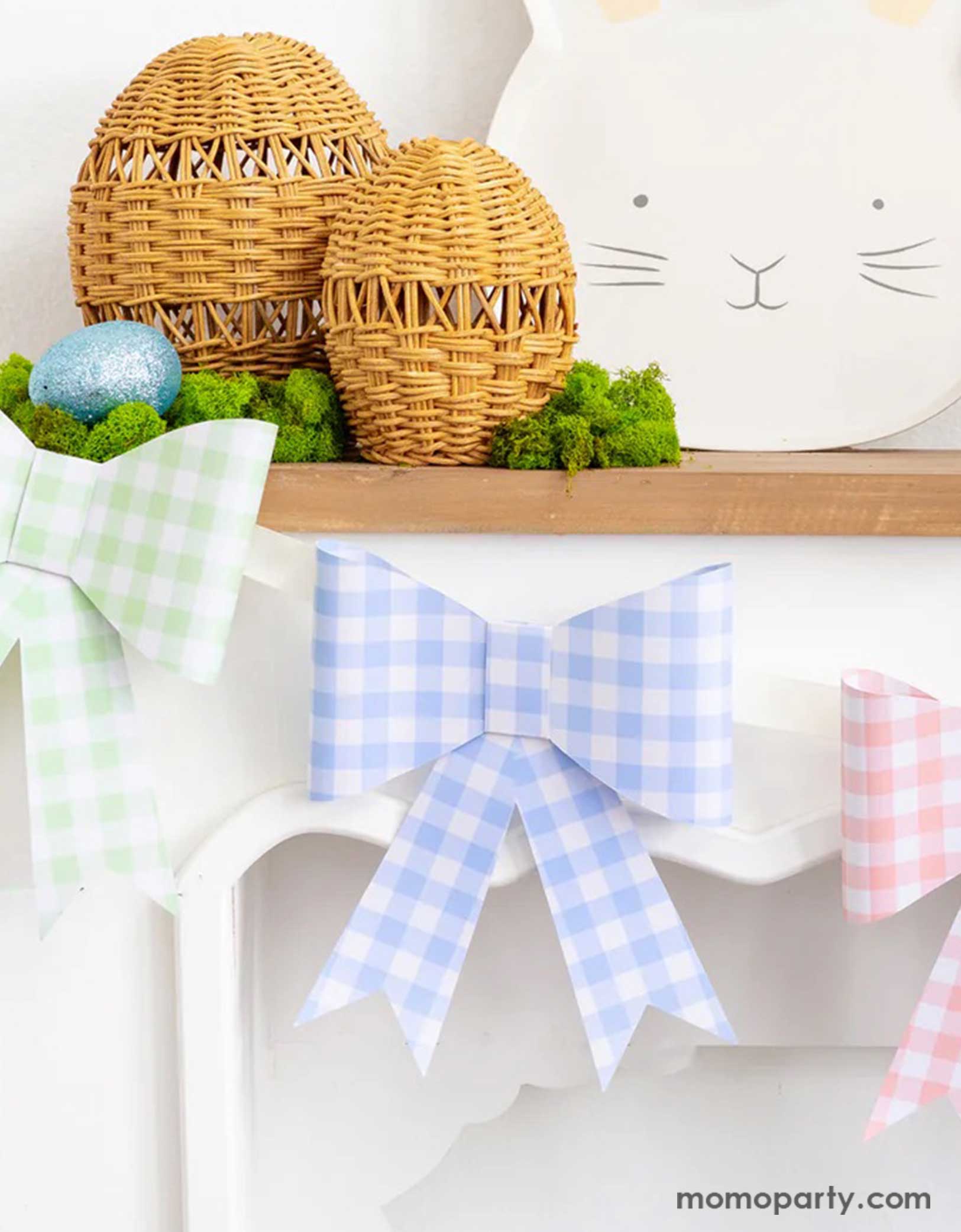 A close-up shot of a mantel decorated with Easter decors including Momo Party's pastel gingham checkered bow party banner, Easter bunny shaped bamboo serving tray and some woven Easter egg decors, along with a basket filled with Easter eggs and spring floral bouquet, a simple yet adorable idea for spring home decor.