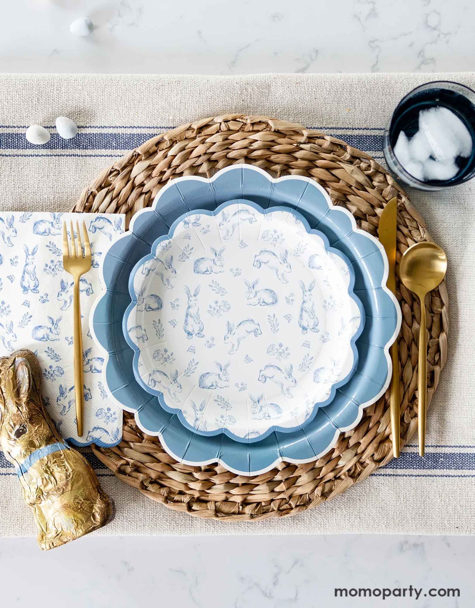 An elegant Easter tablescape with a clean marble table featuring Momo Party's Bunny Toile Collection including The Blue Scalloped Plate, the Bunny Toile Plate and the Bunny Toile Guest Towel by My Mind's Eye. With the gold cutlery set and chocolate bunny and easter egg candies around, this makes great inspiration for a modern and elegant placeset for a Easter gathering this spring season.