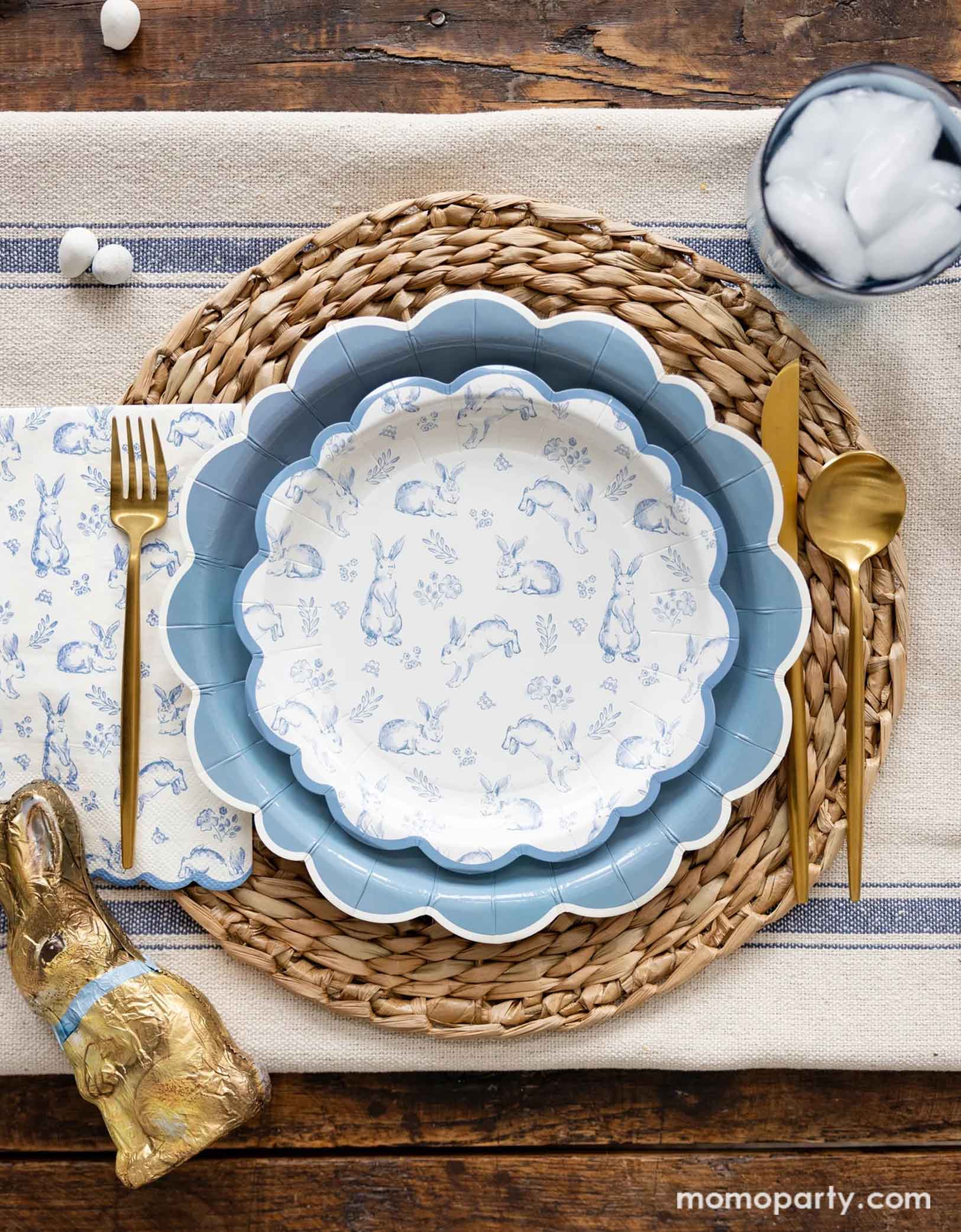An elegant Easter tablescape with a rustic styled background featuring Momo Party's Bunny Toile Collection including The Blue Scalloped Plate, the Bunny Toile Plate and the Bunny Toile Guest Towel by My Mind's Eye. With the gold cutlery set and chocolate bunny and easter egg candies around, this makes great inspiration for a modern and elegant placeset for a Easter gathering this spring season.