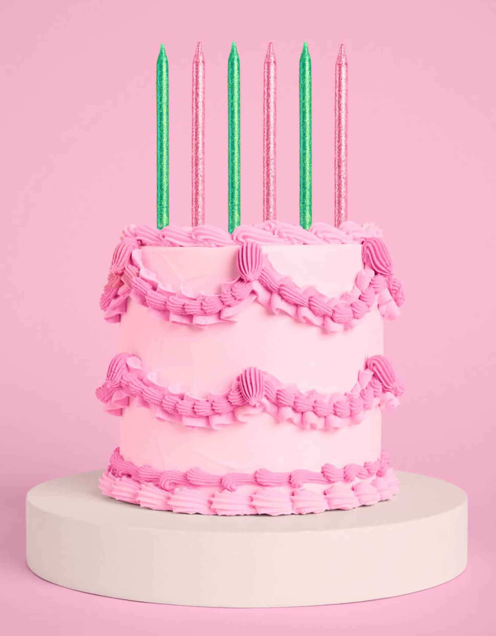 A pink buttercream cake with Momo Party's Wicked Party Emerald City Glitter Candles in pink and green by Xo, Fetti on a pink background.
