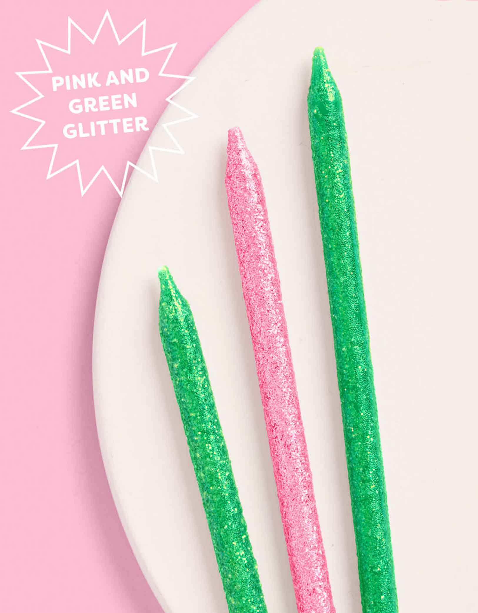 Three glittery candles in pink and green on a white plate with a pink background.