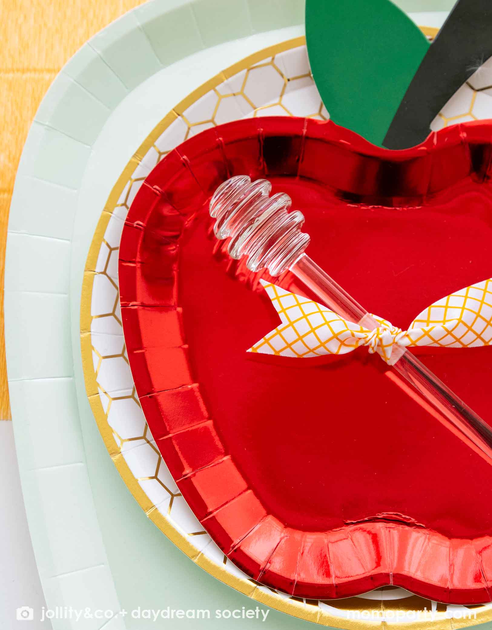Momo Party's red apple shaped plate with a honey dipper on a honeycomb plate and a light green plate.