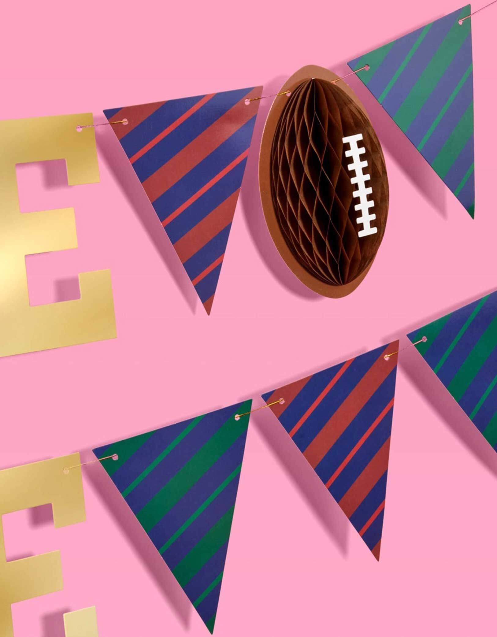 A close up shot of Momo Party's 4.5' football gold foil game time banner with football honeycomb details on a pink background.