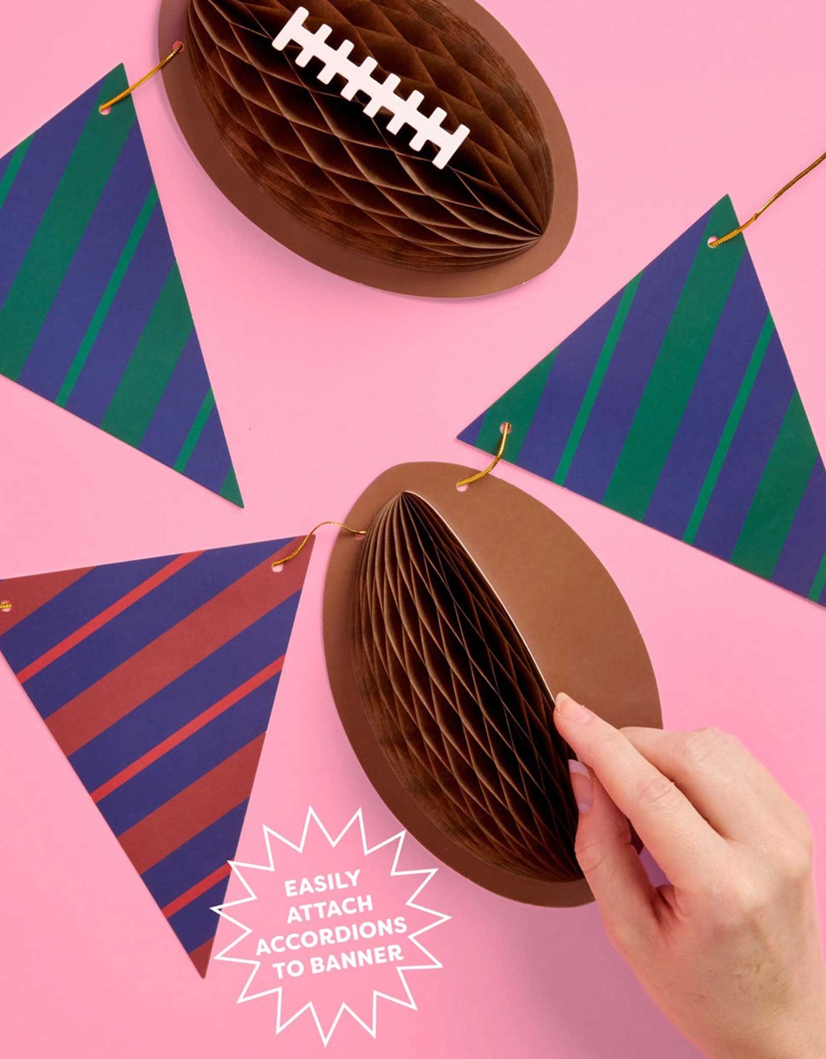 A close up shot of Momo Party's 4.5' football gold foil game time banner with football honeycomb on a pink background.