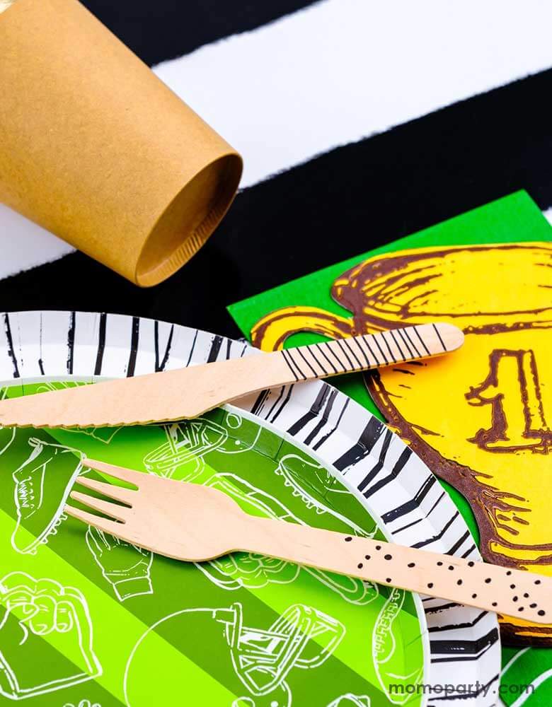A closer look of a modern yet festive football party tablescape featuring football themed tableware from Momo Party including the football shaped paper placemat, the touchdown dessert plates, the trophy shaped napkins on a black striped table runner, making this a perfect inpo for a kid's football themed birthday party or a Superbowl party table decoration.