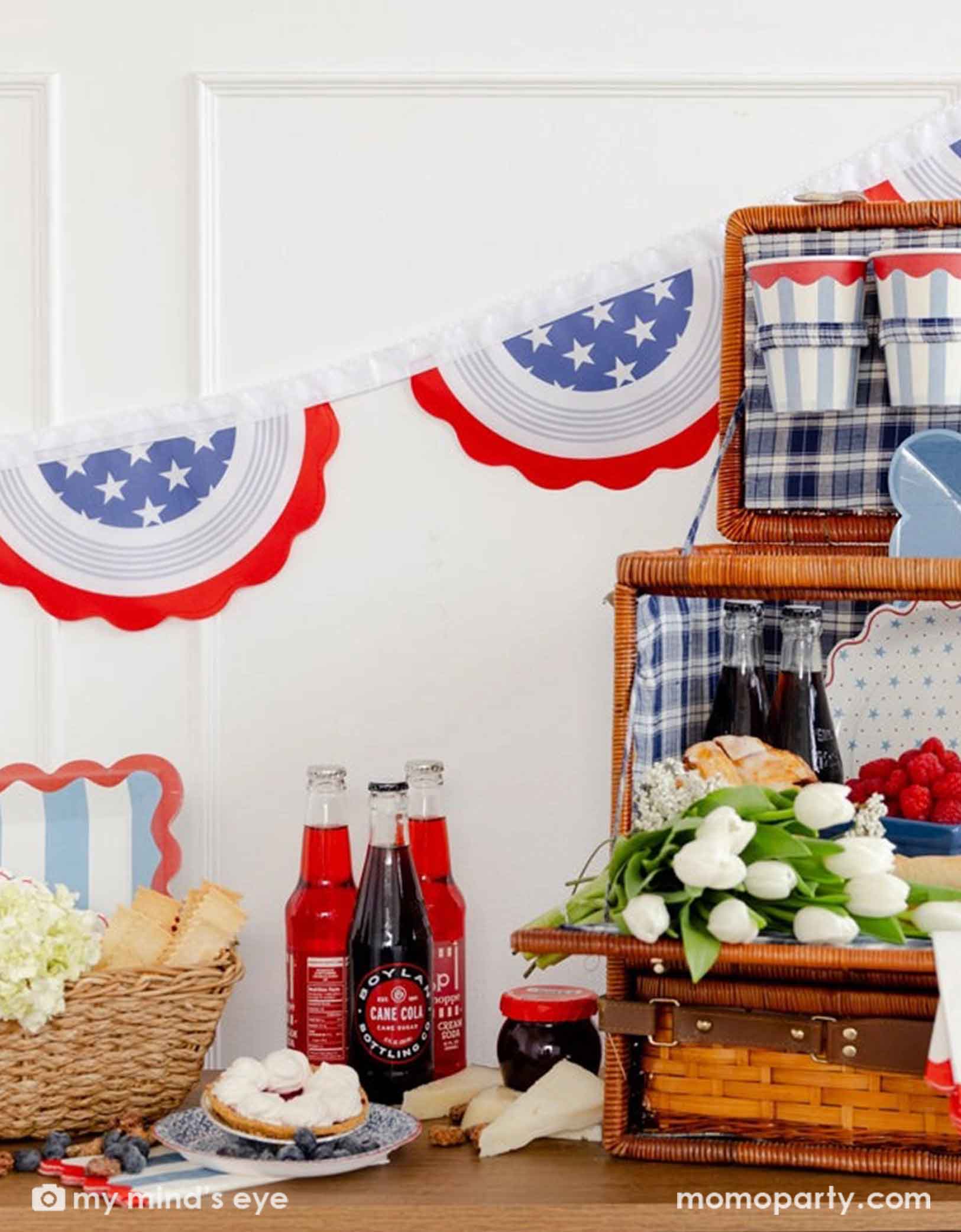 A American themed picnic setup with red, white, and blue decorations, bottles, and food on a table.