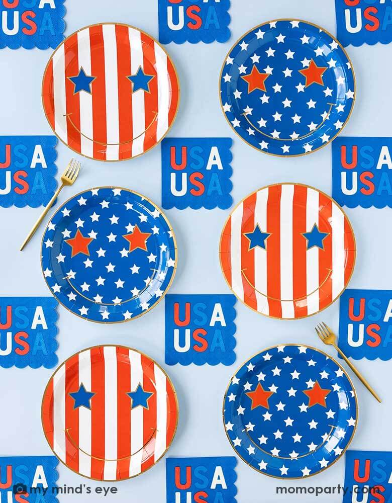 A light blue table features Momo Party's Star & Stripe Smiley Paper Plates by My Mind's Eye. These plates come in a set of 8 in 2 designs, one with red stripes the other with blue stars. With a big smiley face and star eyes on them. Pair with 5" USA small blue napkins, they are perfect for a retro fun 4th of July party this summer!
