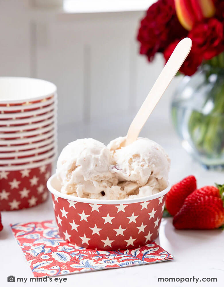 Momo Party's red star sundae cup by My Mind's Eye with a couple of scoops of ice cream in it. Underneath the sundae cup is the Hampton floral napkin. On the table there's a red bouquet and some strawberries around.