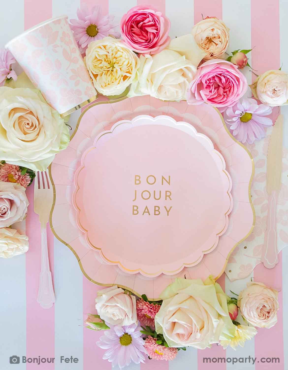 An overhead shot of a pastel pink themed baby girl shower tablescape with baby pink plates, wooden utensils and bunch of flowers around on Momo Party's petal pink striped table runner.