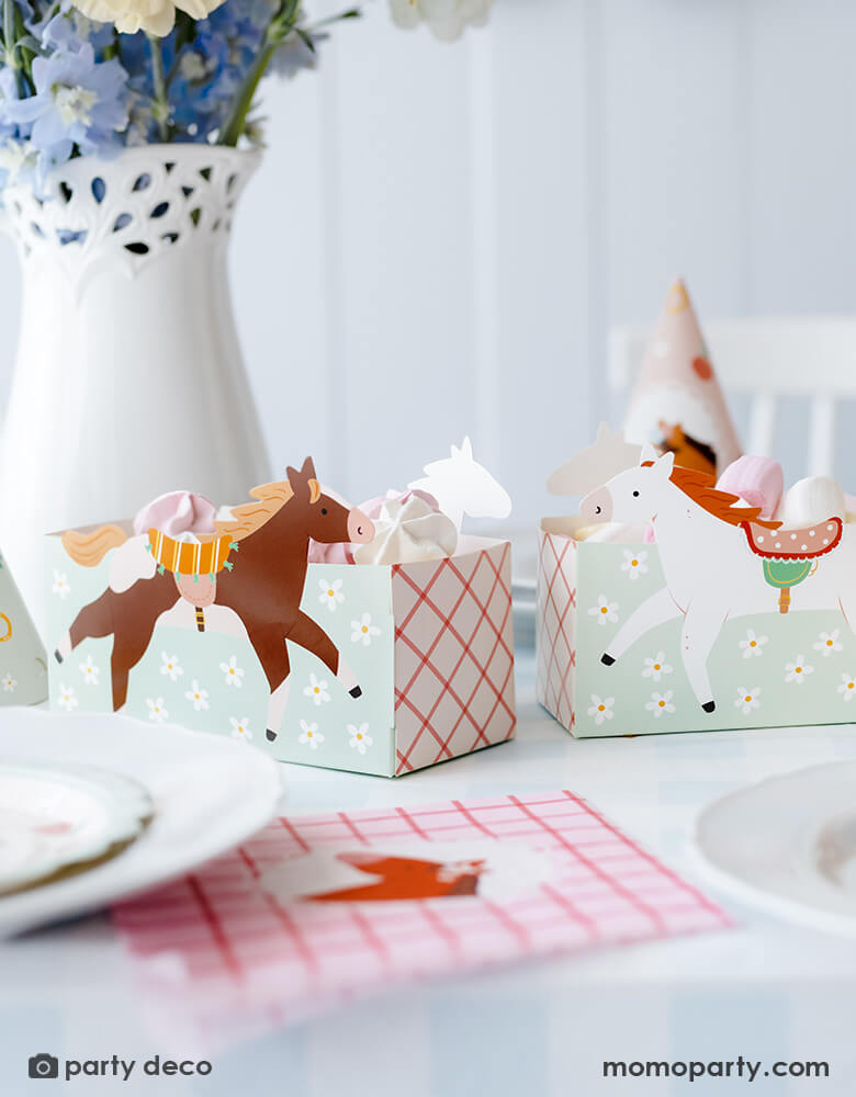 A horse/pony themed birthday party table features Momo Party's 6.7" x 4.3" x 2.95" floral pony treat boxes by Party Deco. Each snack box has some delicious treats in them including cookies and macarons. Behind the treat boxes is a beautiful flower arrangement and some party hats. In front of the snack boxes is a place setting features a pink gingham pony napkin - a darling inspo for girl's pony themed party.