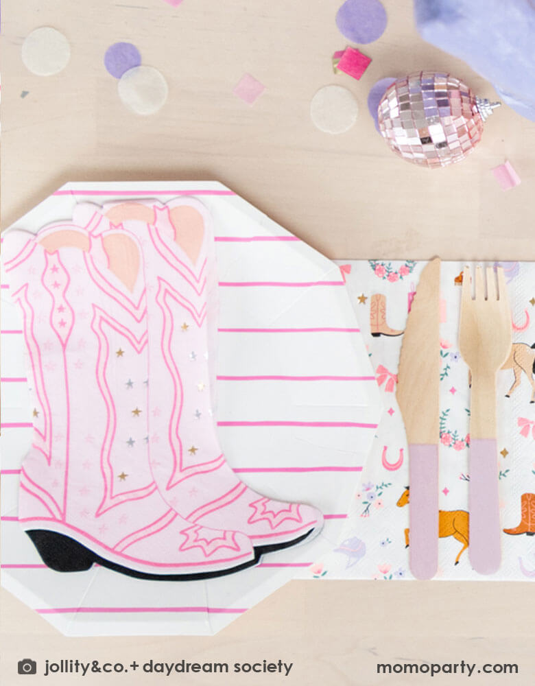 A girly cowgirl rodeo Western themed party table feature Momo Party's cowgirl boots shaped napkins, pink striped party plates, light pink wooden cutlery and cowgirl motif large napkins by Daydream Society. Around the tableware there are some lilac round confetti spread-out and a small pink disco ball decoration, making this an adorable inspiration for girl's First Rodeo first birthday celebration or an adorable cowgirl theme party for pony-loving girls!