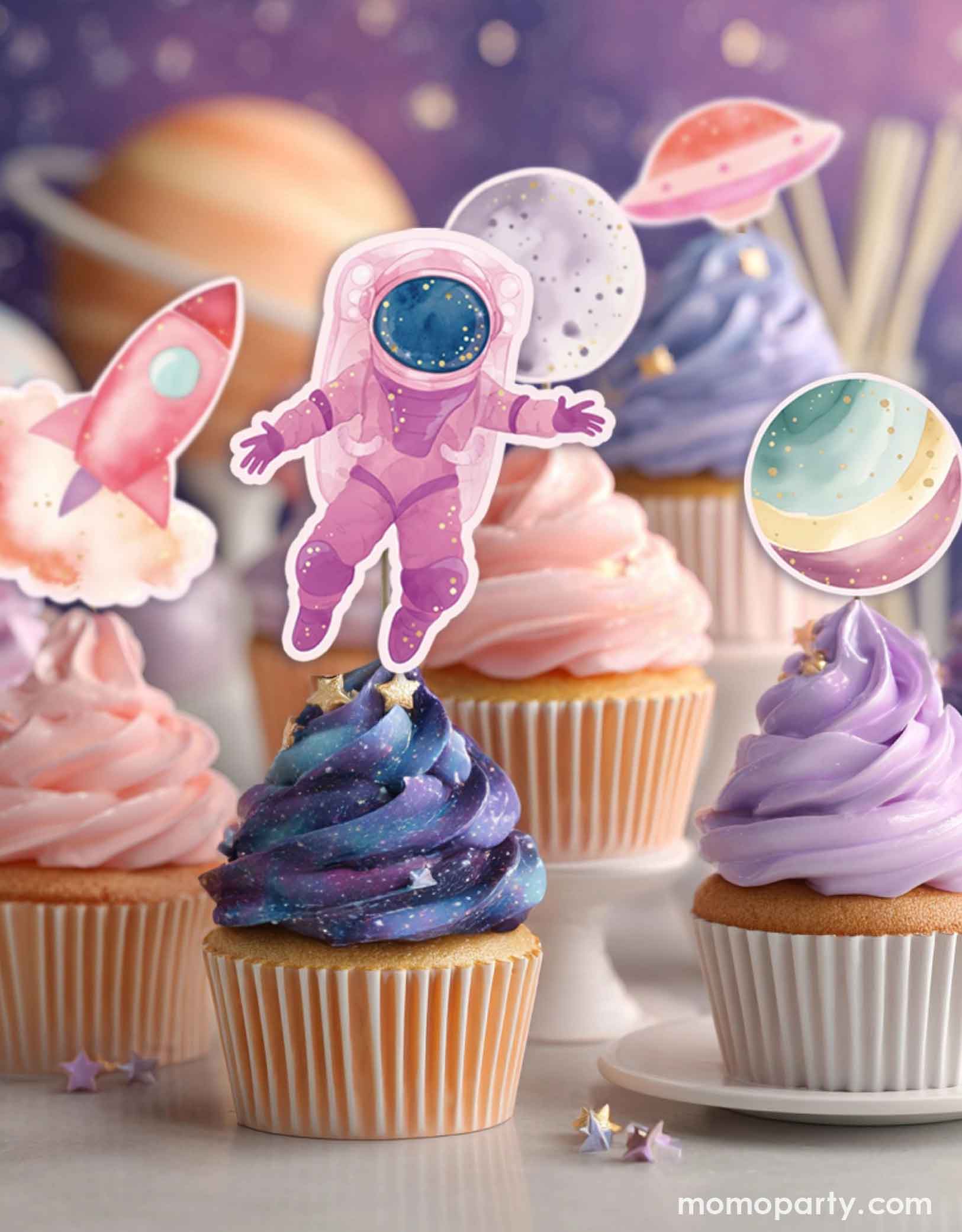 Pastel galaxy themed cupcakes in lilac, pink and galaxy blue with sprinkles with Momo Party's space-themed cupcake toppers including an astronaut, rocket, and planets on a galaxy themed background at a girl's space birthday party.