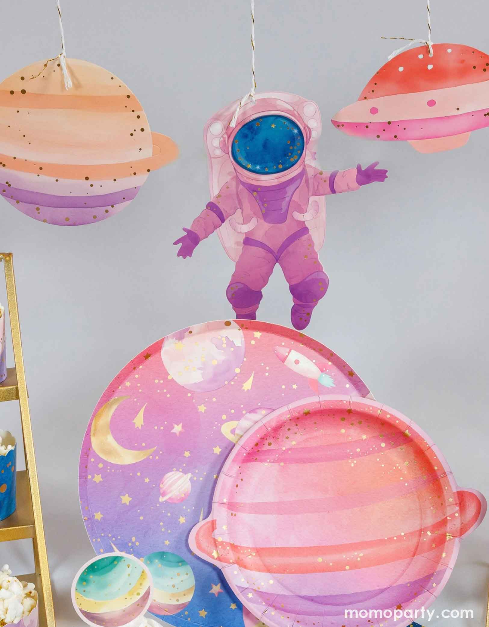 A table with Momo Party's colorful space-themed party plates and cupcakes. Above it hung the astronaut girl space garland set strung with space-themed paper pennants including planets, stars, and a pink astronaut.