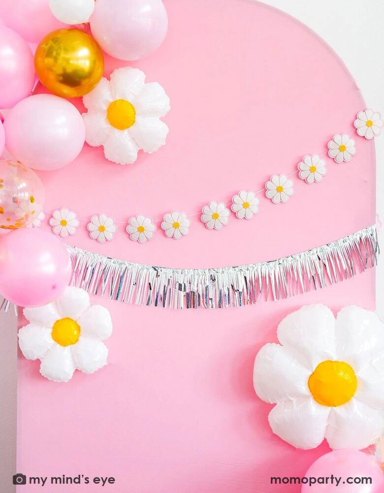 A pink wooden party backdrop wall decorated with Momo Party's daisy felt banner and silver fringe banner set. Around it are a organic balloon garland in pink, white and gold colors, with some daisy shaped foil balloons in different sizes, making this a perfect inspo for a festive and adorable decoration for kid's daisy themed birthday party or a retro inspired bash!