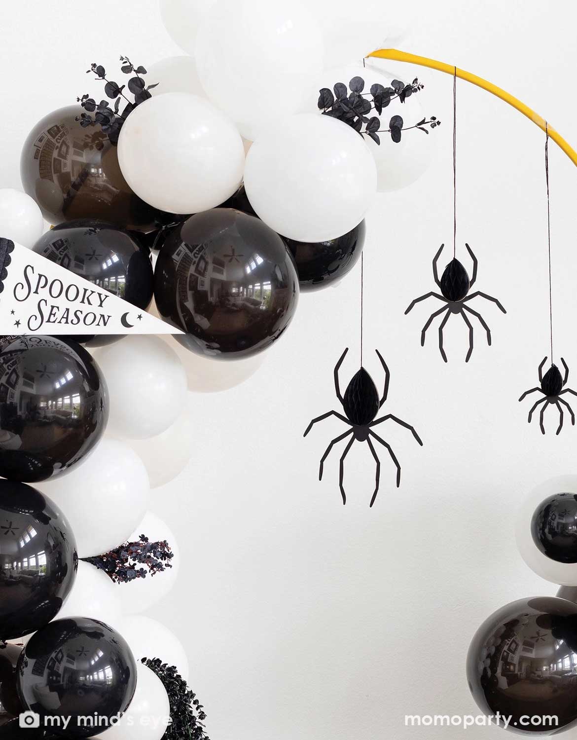 Spooky Halloween balloon garland decoration with black and white balloons, Momo Party's black spider honeycomb decorations hanging from a yellow balloon arch, and a 'Spooky Season' banner.
