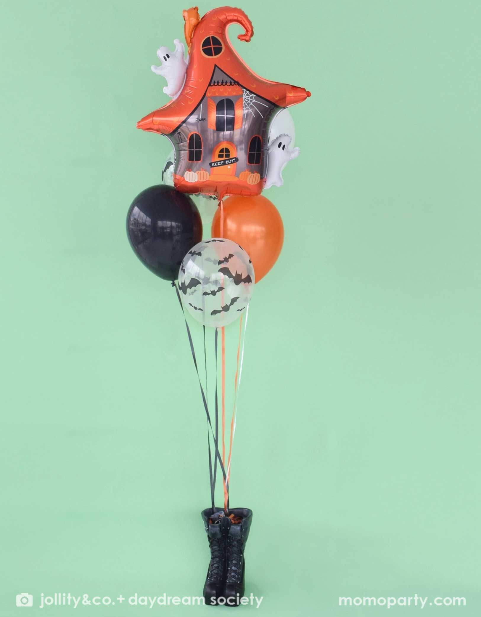 Momo Party's 23.4" x 24.8" Halloween themed balloon shaped like a haunted house with ghosts by Daydream Society with a mix of Halloween themed latex balloons in orange, black and bat design attached to a pair of witch boots on a mint green background.