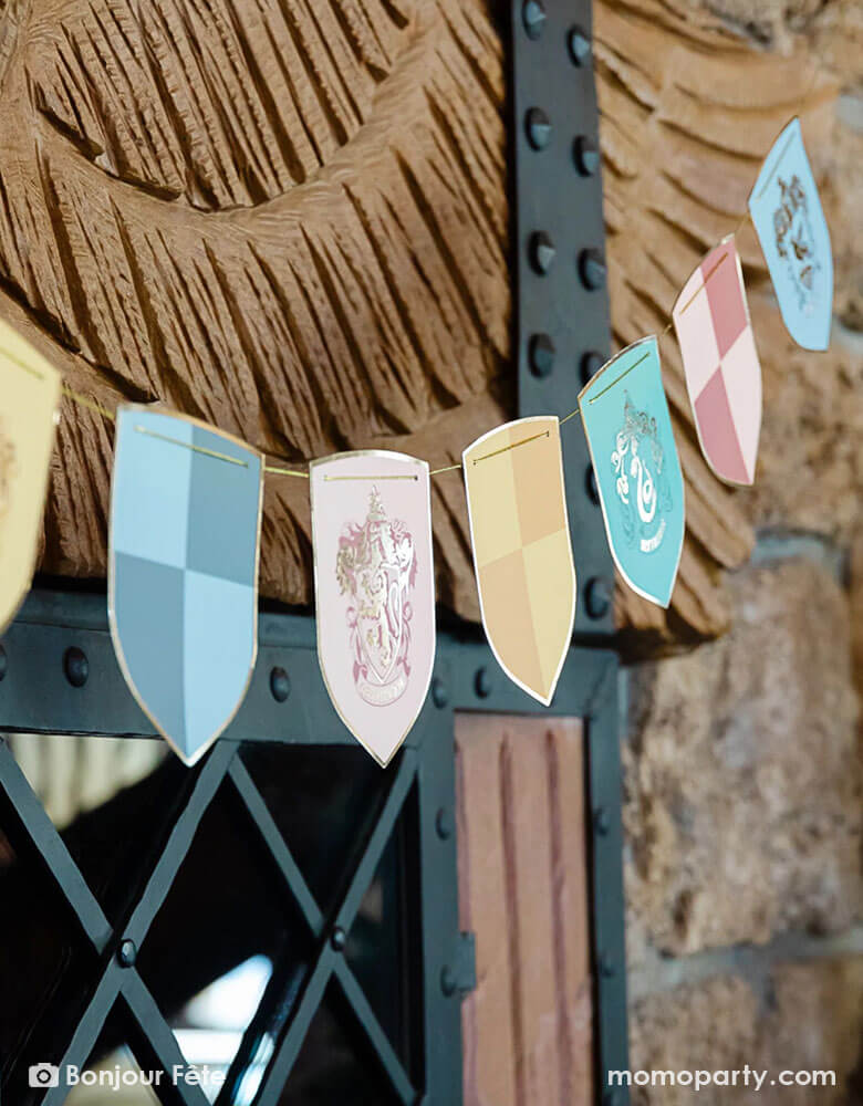 A close up shot of Momo Party's Harry Potter school pride multicolor party banner featuring different Harry Potter house symbols and colors including Hufflepuff, Slytherin, Gryffindor and Ravenclaw hung on outdoor on a brick wall at a Harry Potter themed party.