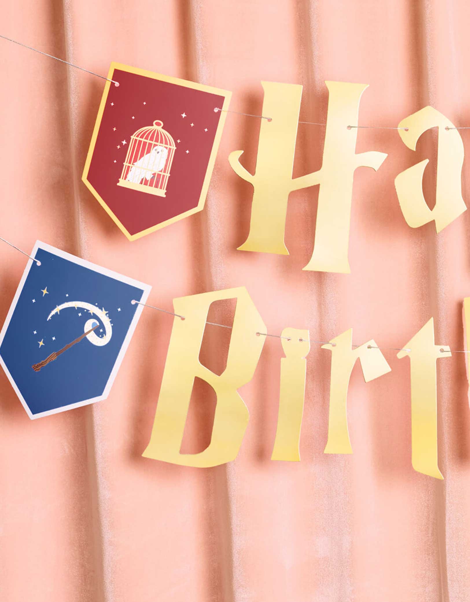 Momo Party's 5' Harry Potter themed Wizard Birthday Party Banner by Xo, Fetti. Inspired by the Hogwarts in Harry Potter, this party banner features "Happy Birthday" letters with red, green, blue and yellow Harry Potter colored house crest shaped pendants with designs of an owl, a wand, a spell book, and a cauldron. It's perfect for kid's Harry Potter themed birthday party!