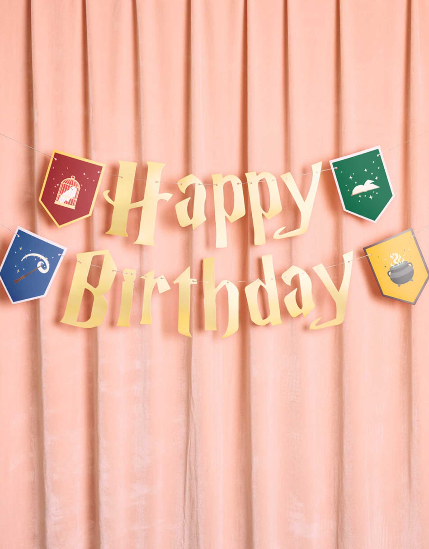 Momo Party's 5' Harry Potter themed Wizard Birthday Party Banner by Xo, Fetti. Inspired by the Hogwarts in Harry Potter, this party banner features "Happy Birthday" letters with red, green, blue and yellow Harry Potter colored house crest shaped pendants with designs of an owl, a wand, a spell book, and a cauldron. It's perfect for kid's Harry Potter themed birthday party!
