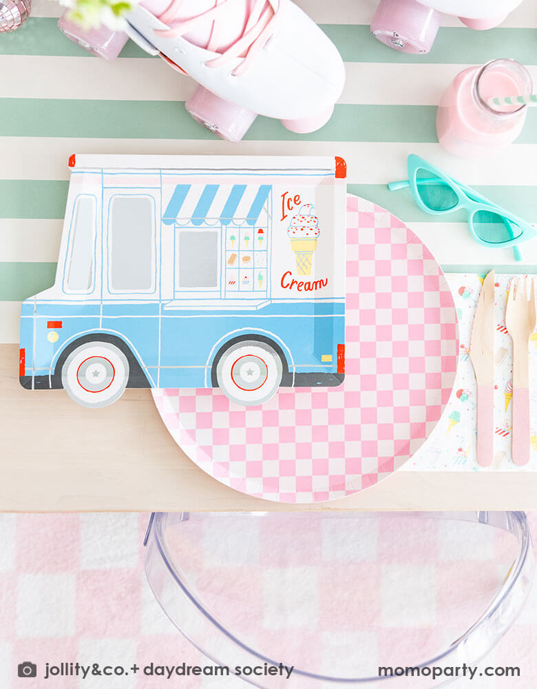 An adorable kid's ice cream themed birthday party tablescape featuring Momo Party's ice cream truck shaped plate, the pink checkered plate, the ice cream icon napkin and pink wooden cutlery on a mint striped table runner. Around the placeset there are some summer inspired decoration like a pair of mint sunglasses, a pair of pink roller skates, some milk bottles with gum ball pink drinks, making this a cute, fun and festive ice cream social for friends and family!
