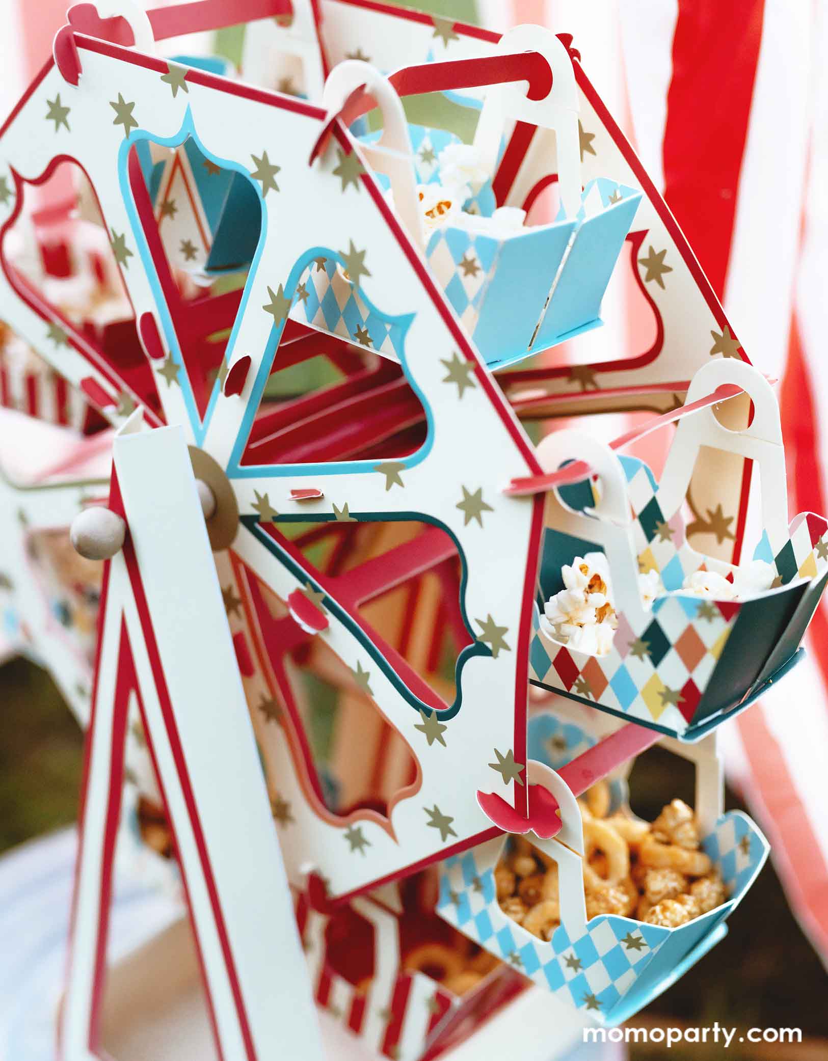 A close up shot of Momo Party's 18.9" x 19.7" Carnival Ferris Wheel Snack Stand by Party Deco. This stunning centerpiece with its circus-inspired design is loaded with treats and cupcakes and they kids are grabbing the goodies from this fun treat stand.