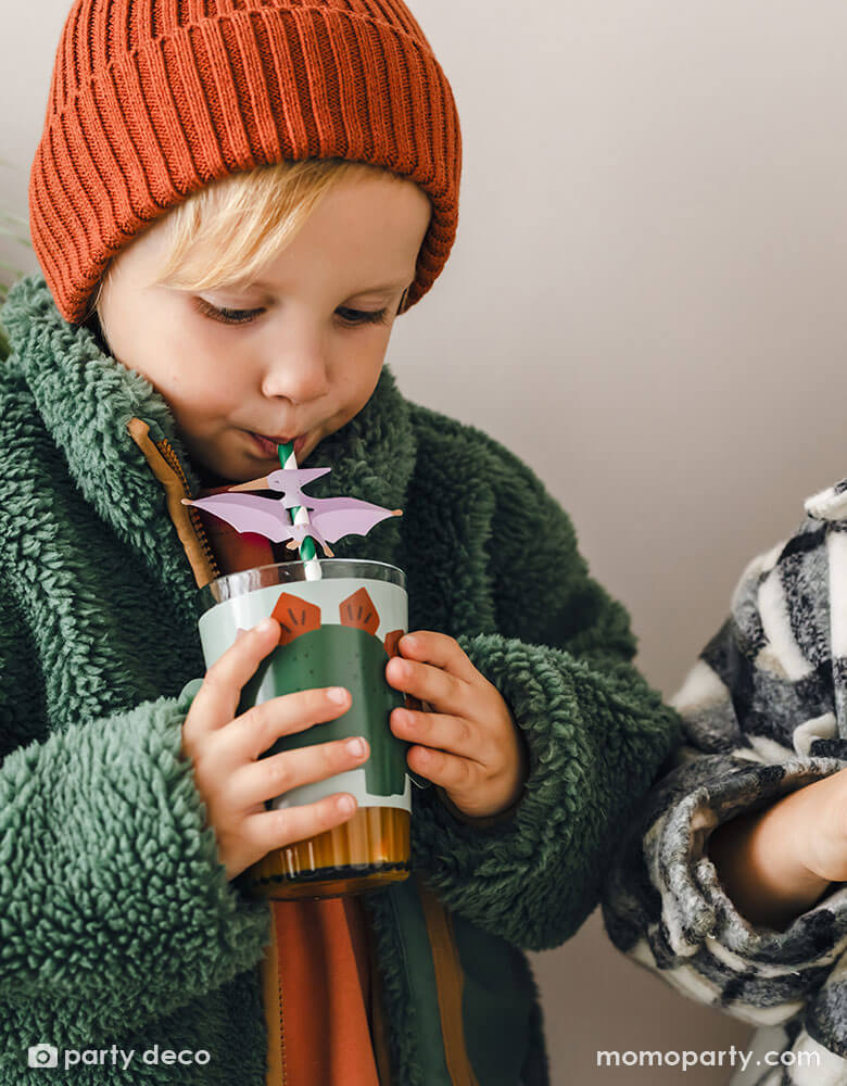 A boy sipping a cup wrapped with dinosaur cup sleeve using Momo Party's Pterodactyl striped straw at a dinosaur themed birthday party.